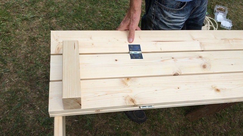 How Do You Build A Sandbox With A Lid And Bench? 2 Blick auf eine Holzkonstruktoin. Eine Hand hält etwas davon fest.