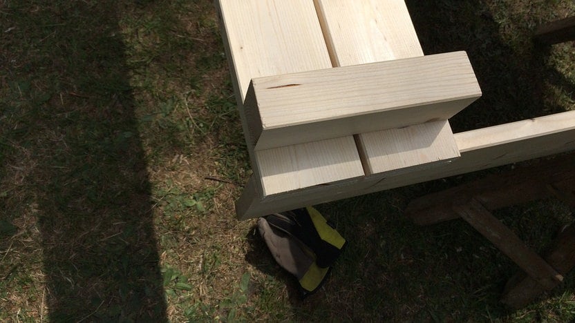 How Do You Build A Sandbox With A Lid And Bench? 1 Blick auf eine undefinierbare Holzkonstruktion. Im Hintergrund ist Wiese und ein herumliegender Arbeitshandschuh zu sehen.