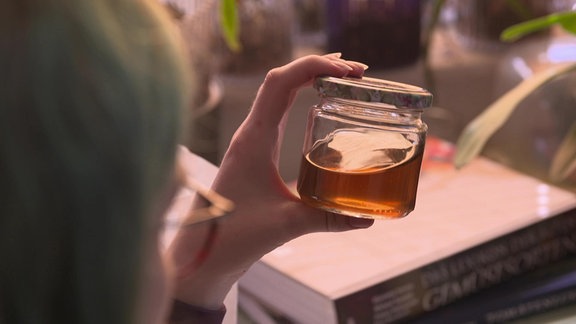 Hand hält ein Glas mit einer goldfarbenen Flüssigkeit.