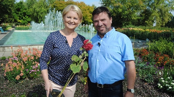 MDR Garten-Moderatorin Diana Fritzsche-Grimmig steht mit einer gefüllt rot blühenden Stockrose im Topf neben Sebastian Albrecht vom Eichsfelder Staudenhof im Erfurter Egapark
