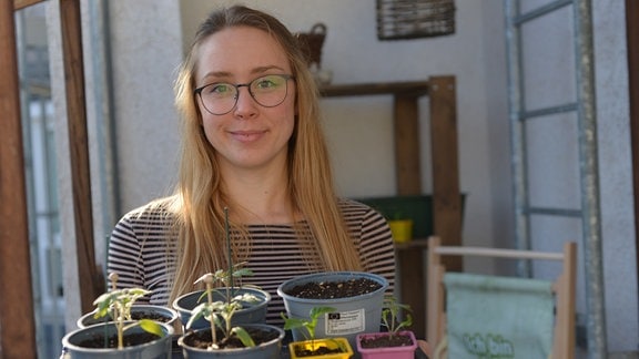 Katharina Koch steht auf ihremn Balkon und hält junge Pflanzen auf einem Tablett