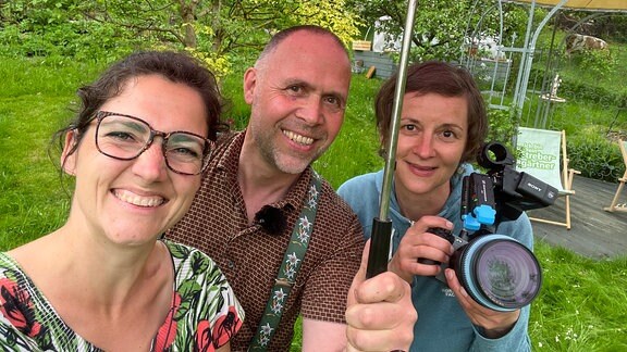 Reporterin Nadine Witt, Strebergärtner Oliver Richter und Kamerafrau Daniela Dufft unter Regenschirm