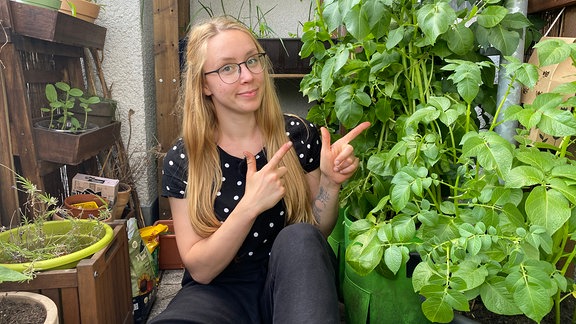 Strebergärtnerin Katharina Koch zeigt auf Pflanzsack mit Kartoffel-Pflanzen