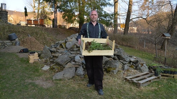 Oliver Richter steht in seinem Garten und hält eine Kiste mit Pflanzen