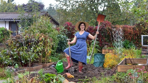 Kleingärtnerin Nadine Witt posiert mit Gartenwerkzeugen auf einem Acker im Kleingarten. 