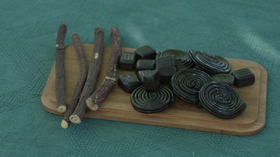 Süßholzwurzelstücke und Lakritzschlangen liegen auf einem Brett.