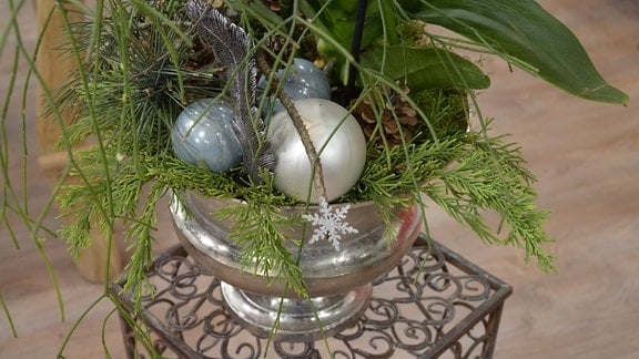 Auf einem Blumentopf liegen Weihnachtsbaumkugeln und Tannengrün. 