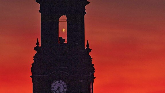 Morgenrot hinter der Dreikönigskirche in Dresden (Ausschnitte zwischen Uhr und Spitze), im Turmfenster ein Herrnhuter Stern der gelb leuchtet