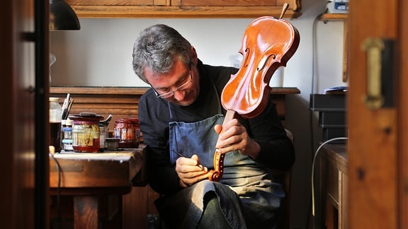 Geigenbaumeister Ekkard Seidl lackiert eine Geige in seiner Werkstatt in Markneukirchen (Sachsen).