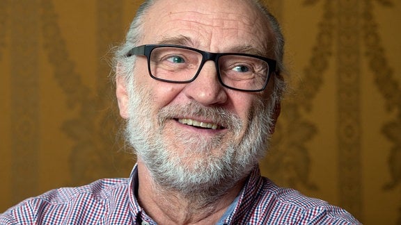 Ein Mann mit grauem Bart und Brille lacht.