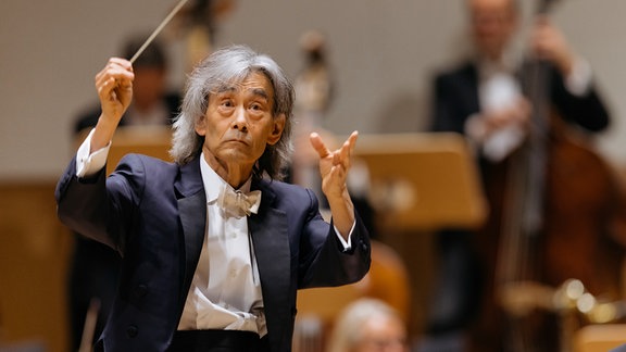 Kent Nagano: Ein Mann gestikuliert mit einem Dirigiertstock vor einem Orchester.