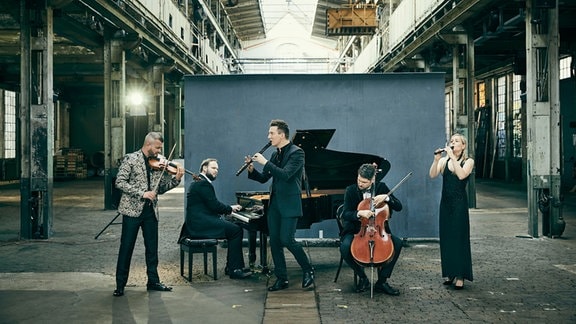 Fünf Musikerinnen und Musiker mit Flügel, Flöten, Geige und Cello in einer alten Fabrikhalle.