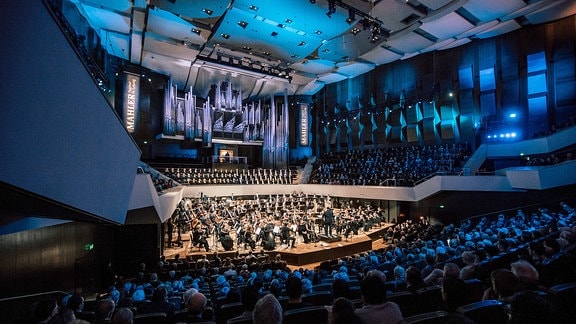 Ein Orchester spielt im Gewandhaus. Es hängen Plakate: Mahler Festival Leipzig