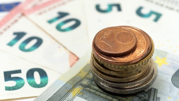 Euromünzen sind auf einem 5-Euroschein aufeinander gestapelt.