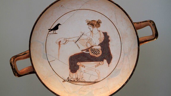 Arbeit eines anonymen Athener Vasenmalers. Auf weißem Grund ist Apollo dargestellt. Seine linke Hand berührt die Saiten seiner Lyra.