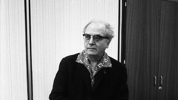 Schwarz-Weiß-Bild von Olivier Messiaen: Ein Mann stützt sich auf einen geschlossenen Flügel.