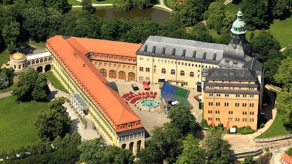 Luftaufnahme Schloss Sondershausen: Eher flaches Schloss im Grünen mit fast dreieckigem Grundriss und Bühne sowie Stühle im Innenhof.