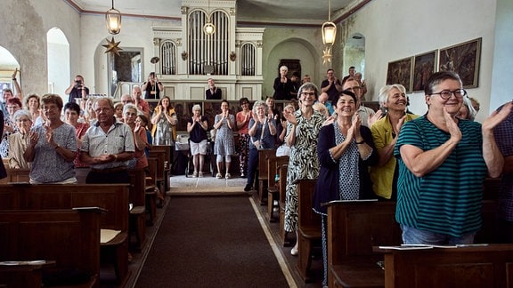 Sommergesang Haferungen: Blick in den Raum einer Kirche mit Bänken und Orgel, Menschen stehen und klatschen, freudige Gesichter 