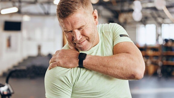 Ein Mann im Gym hält sich die Schulter vor Schmerzen