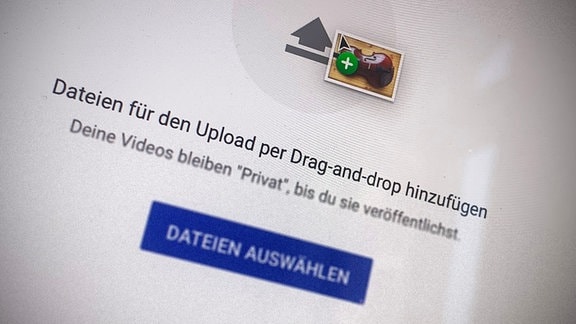 Nahaufnahme Bildschirm, mit Unschärfe-Effekt: Uploadmaske bei YouTube, auf die gerade per Drag'n'Drop eine Datei mit einer Violine im Thumbnail gezogen wird.