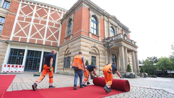 Der rote Teppich wird für die Eröffnung der Bayreuther Richard-Wagner-Festspiele vor dem Festspielhaus auf dem Grünen Hügel befestigt.