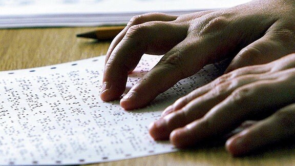 Die Hände eines Blinden lesen ein Blatt mit Braillenoten. 