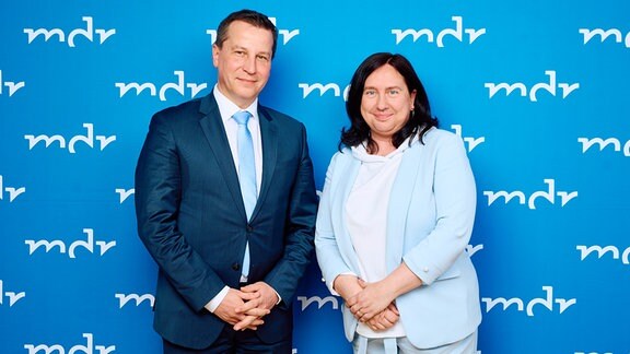 Eine Frau und ein Mann stehen vor einer blauen Wand mit dem Schriftzug MDR.