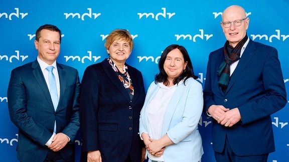 Zwei Frauen und zwei Männer stehen vor einer blauen Wand mit dem Schriftzug MDR.