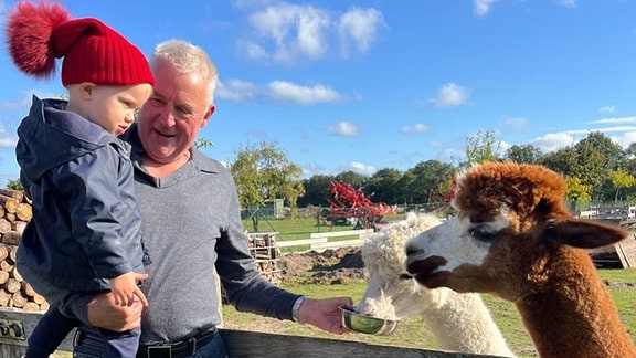 Ein Mann hält ein Kind auf einer Lama Farm