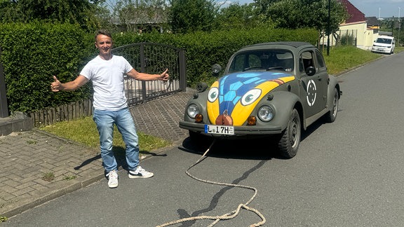 Ein rostiger VW Käfer steht mit Abschleppseil auf einer Straße