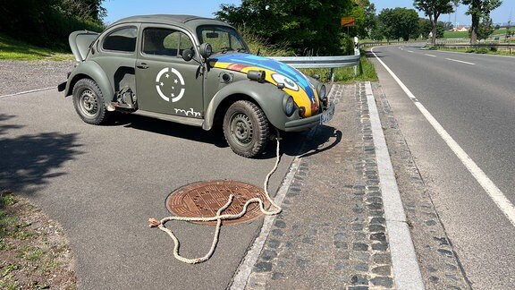 Ein rostiger VW Käfer steht mit Abschleppseil auf einer Straße