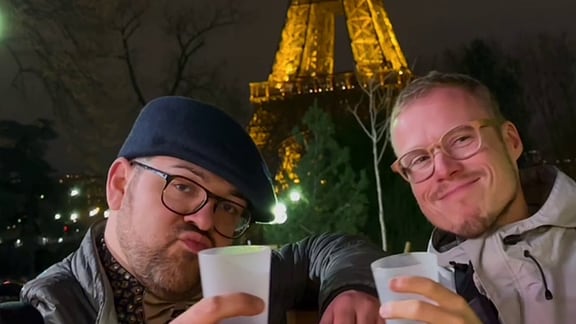 Zwei Männer stehen vorm beleuchteten Eiffelturm in Paris