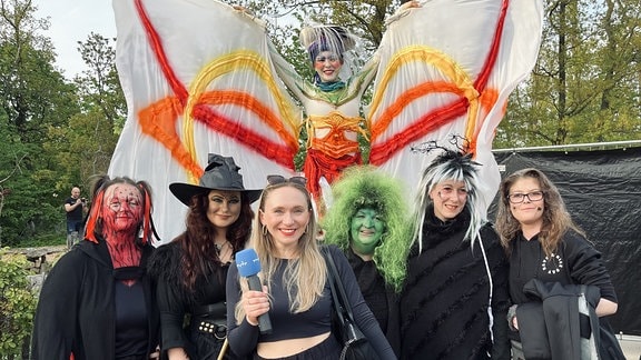 Eine Frau mit Mikrofon in der Hand steht vor mehreren als Hexen verkleideten Frauen