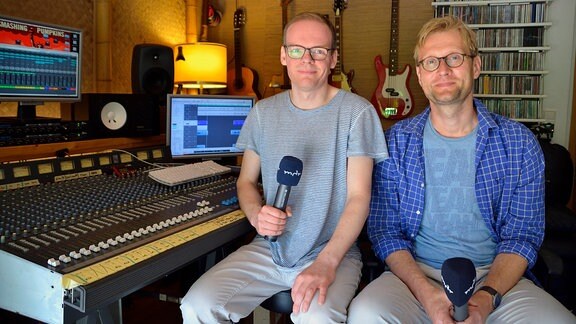 Zwei Männer mit Mikrofonen sitzen nebeneinander in Musikstudio
