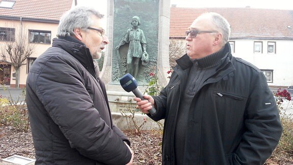 Bürgermeister Gustav Voigt (links)  wird vor dem Lutherbrunnen interviewt.