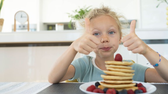 Ein Kind mit Pfannkuchen auf dem Teller hält die Daumen hoch