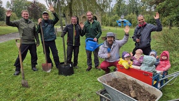 Hüttenrode Mehrere Menschen winken in die Kamera, in einem kleinen Wagen daneben sitzen Kindergartenkinder.