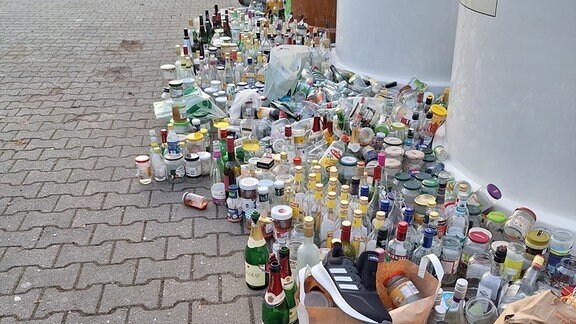 Glascontainer, rundherum zahlreiche leere Flaschen und anderer Müll