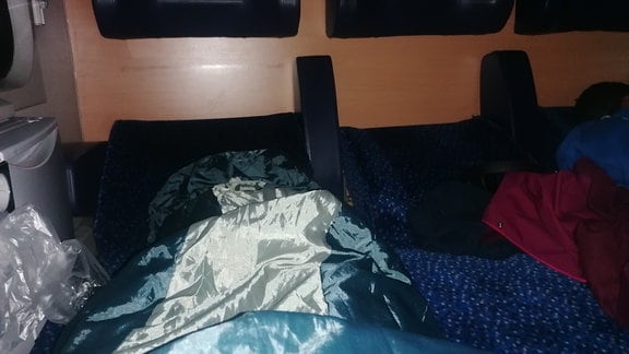 Zusammengeschobene Sitze in einem Sitzwagen, auf denen ein Schlafsack liegt