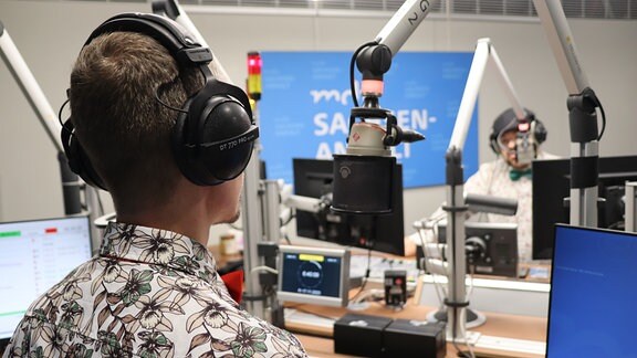 Zwei Männer mit Hemd und Fliege stehen an Mikrofonen in einem Radio-Studio