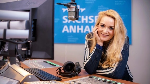 Blonde Frau im Radiostudio lächelt in die Kamera.