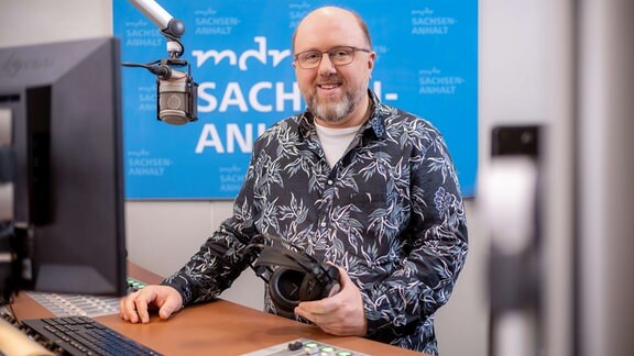Mann mit Glatze und Brille in schwarzem Hemd mit Print in einem Radiostudio