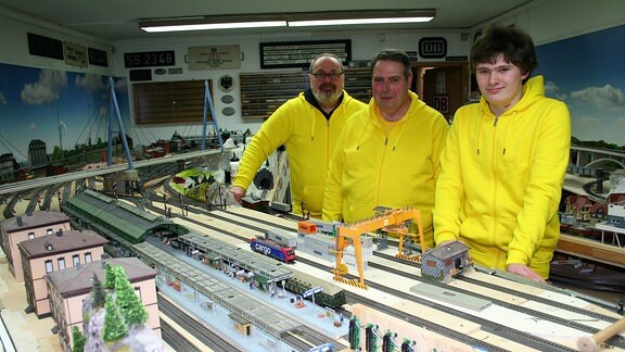 Drei Menschen stehen vor einer Miniatureisenbahn-Anlage