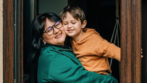 Eine Frau mit Brille trägt ein Kind auf dem Arm.
