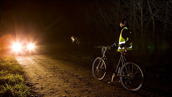 Ein Radfahrer mit Warnweste begegnet in der Dunkelheit einem Pkw