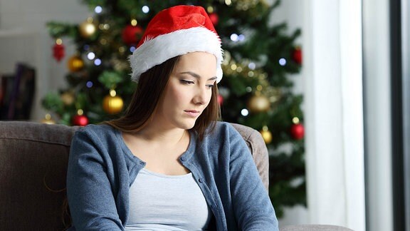 Eine Frau mit Weihnachtsmütze, sitzt alleine auf der Couch.