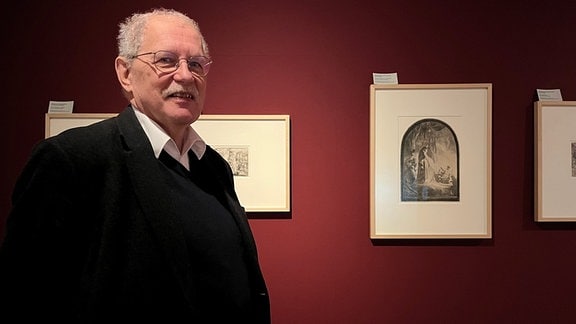 Ein Mann mit Brille steht vor Zeichnungen des bekannten Malers Rembrandt