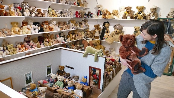 Eine Frau mit einem Teddybär in der Hand in einem Raum voller Teddys im Spielzeugmuseum Sonneberg