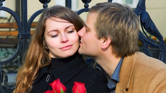Junger Mann mit Rosen in der Hand küsst eine junge Frau.