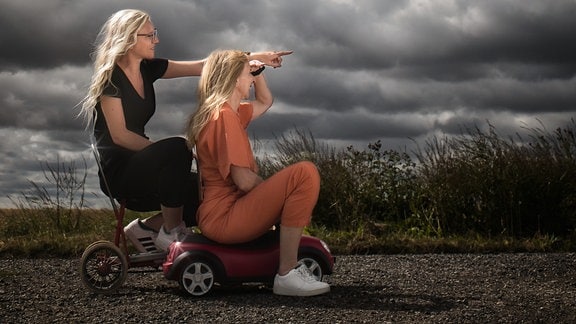 Zwei Frauen mit Bobbycar auf der Straße, darüber der Titel Blechbezaubert